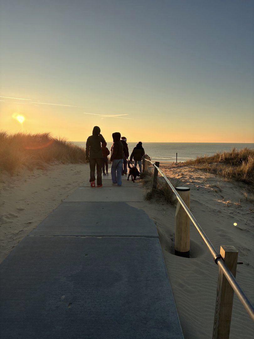 Familie wandelt over duinpad bij zonsondergang