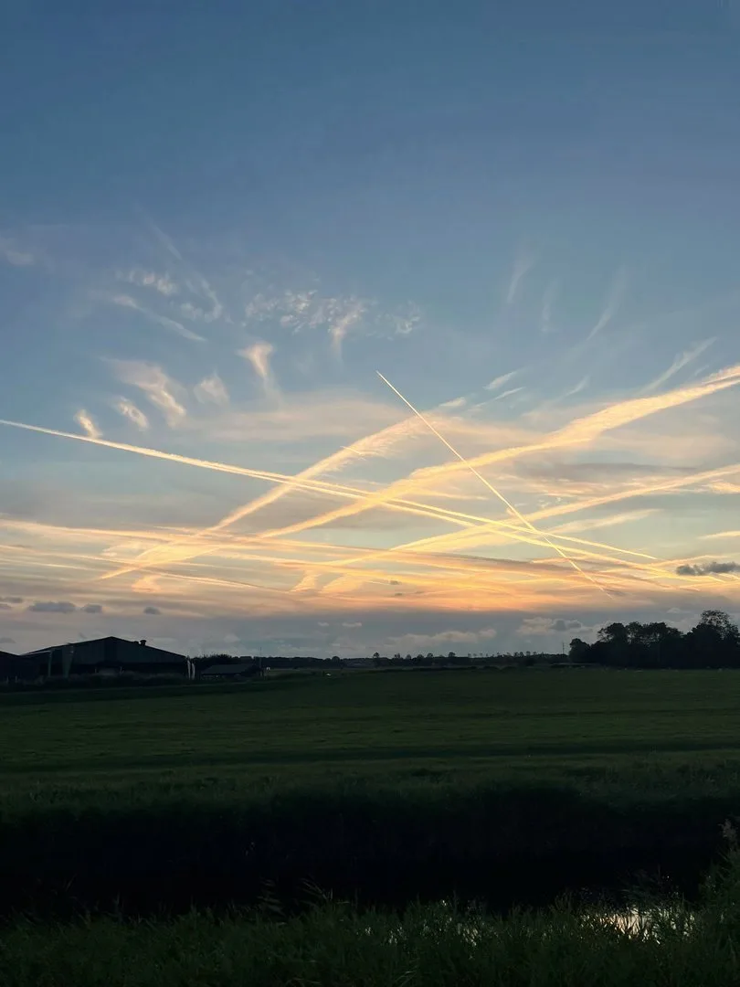 Avondlucht met wolkenstrepen boven een weiland en boerderij